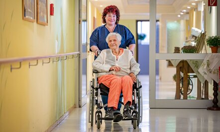 Pflegerin schiebt Bewohnerin im Rollstuhl